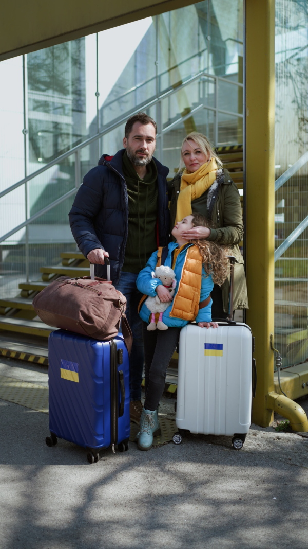 Ukrainian refugee family with luggage at railway station hugging and saying goodbye, a vertical footage.