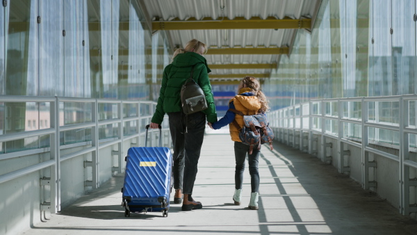 A rear view of Ukrainian immigrant mother with child with luggage walking at train station, Ukrainian war concept.