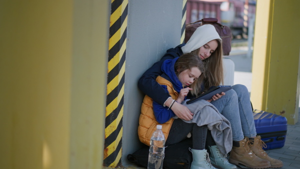 An Ukrainian immigrants sitting and waiting at railway station, using tablet.