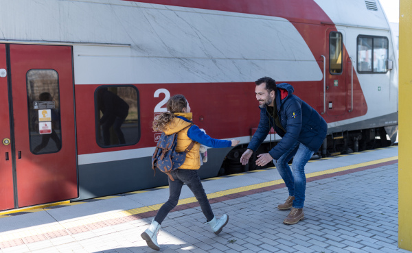 A happy Ukrainian refugee girl running to her father waiting at railway station, reunion after war.