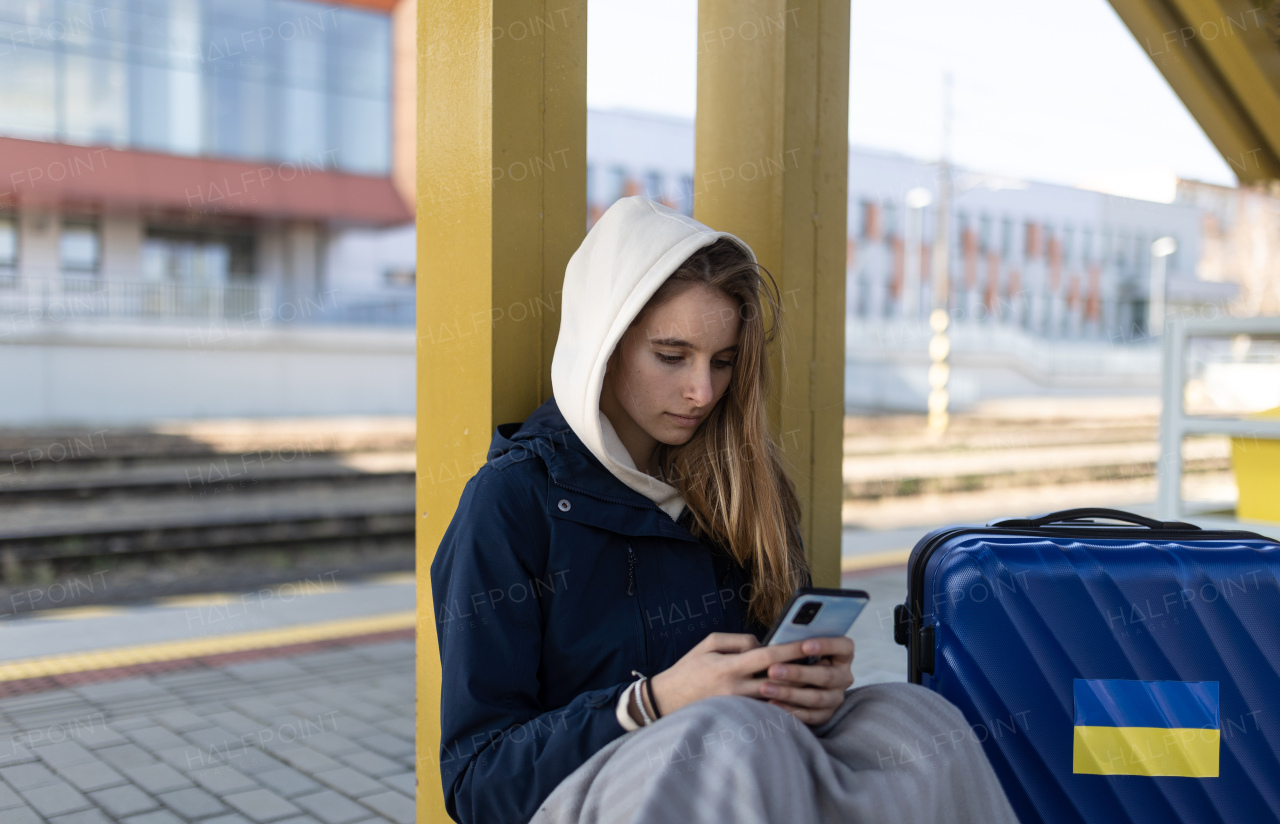 A depressed Ukrainian immigrant young woman sitting and waiting at railway station.