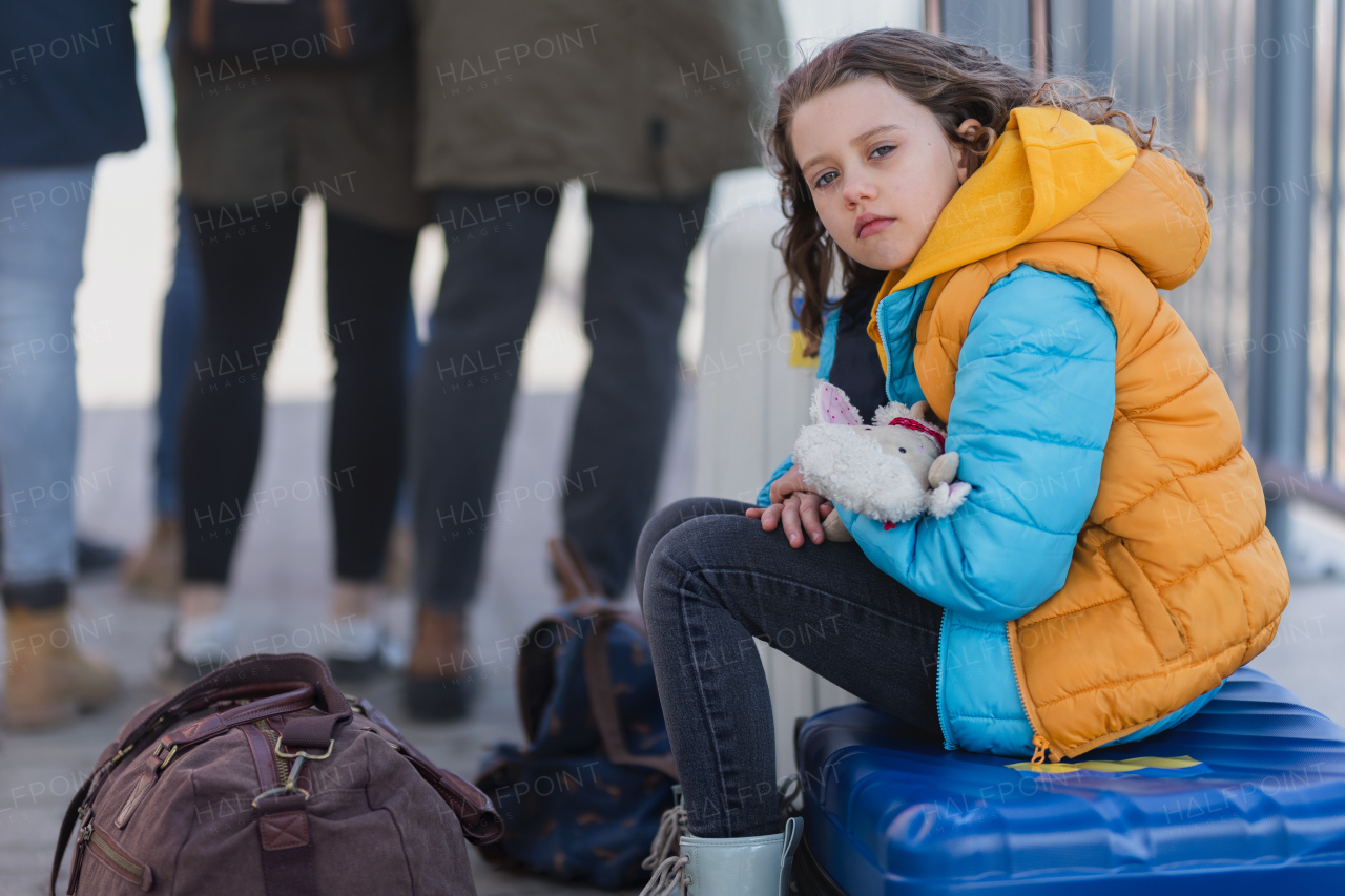 A sad Ukrainian immigrant child with luggage waiting at train station, Ukrainian war concept.