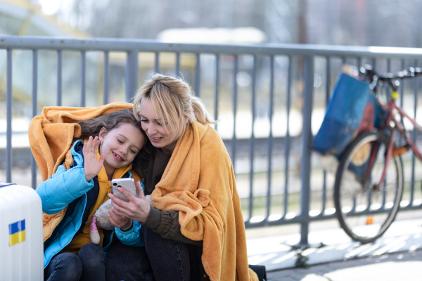 An Ukrainian immigrants mother with daughter with luggage waiting at train station, Ukrainian war concept.