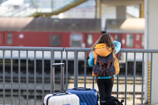 A rear view of Ukrainian immigrant child with luggage waiting at train station, Ukrainian war concept.