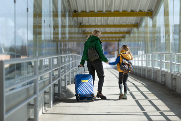 A rear view of Ukrainian immigrant mother with child with luggage walking at train station, Ukrainian war concept.