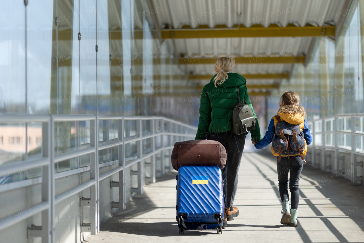 A rear view of Ukrainian immigrant mother with child with luggage walking at train station, Ukrainian war concept.