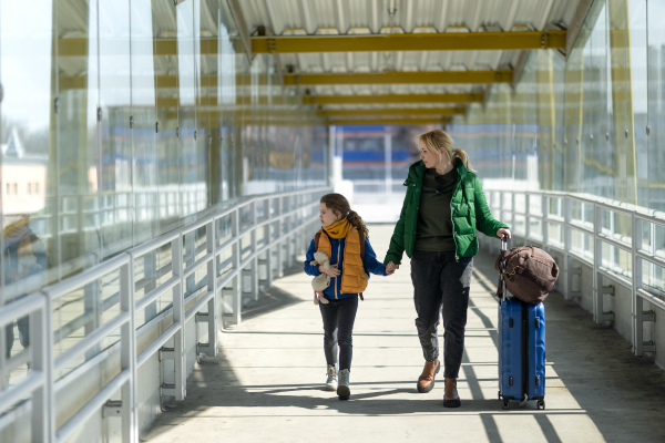 An Ukrainian immigrant mother with child with luggage walking at train station, Ukrainian war concept.