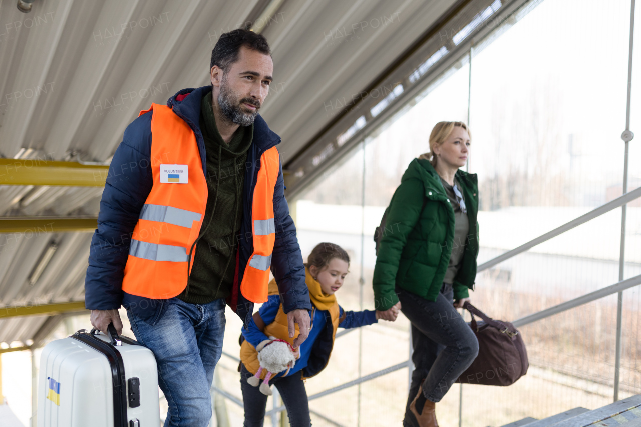 A volunteer helping Ukrainian mother with child, refugees, at train station.