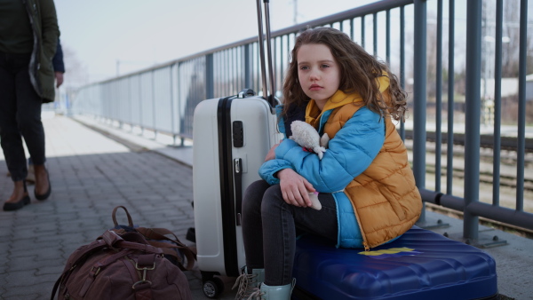 A sad Ukrainian immigrant child with luggage waiting at train station, Ukrainian war concept.