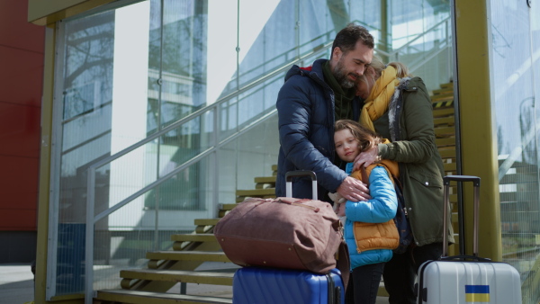 An Ukrainian refugee family with luggage at railway station hugging and saying goodbye, Ukrainian war concept.