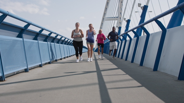 A group of young and old people running outdoors on bridge in city.