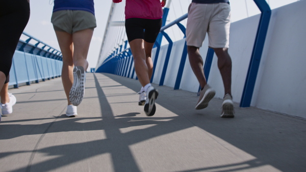 A rear view of group of young and old people running outdoors on bridge in city, lowsection.