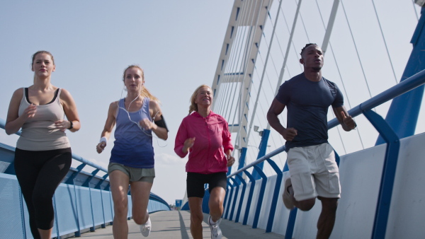 A group of young and old people running outdoors on bridge in city.