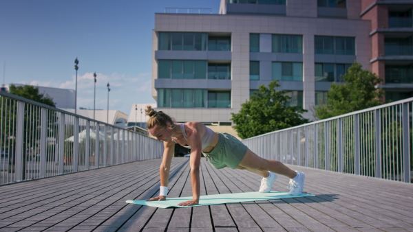 Mid adult woman doing exercise on a mat outdoors in city, healthy lifestyle concept.