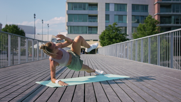 Mid adult woman doing exercise on a mat outdoors in city, healthy lifestyle concept.