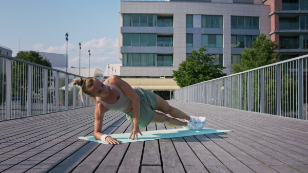 Mid adult woman doing exercise on a mat outdoors in city, healthy lifestyle concept.