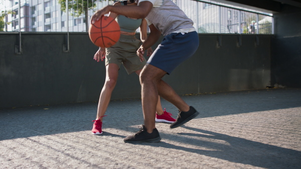 A lowsection of man and woman friends playing basketball outdoors in city.