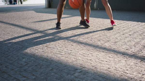 A lowsection of man and woman friends playing basketball outdoors in city.