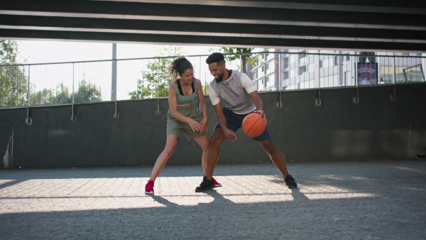 A man and woman friends playing basketball outdoors in city.