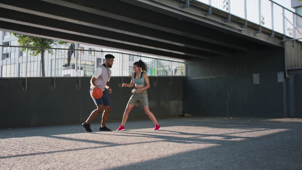 A man and woman friends playing basketball outdoors in city.