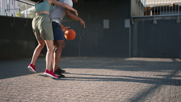 A lowsection of man and woman friends playing basketball outdoors in city.