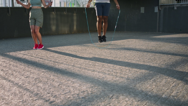 Happy man and woman couple friends doing workout exercise outdoors in city, skipping.