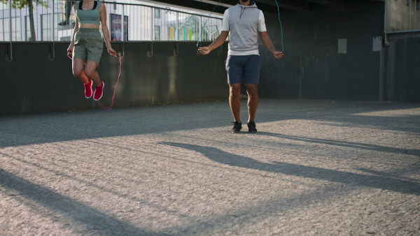 Happy man and woman couple friends doing workout exercise outdoors in city, skipping.