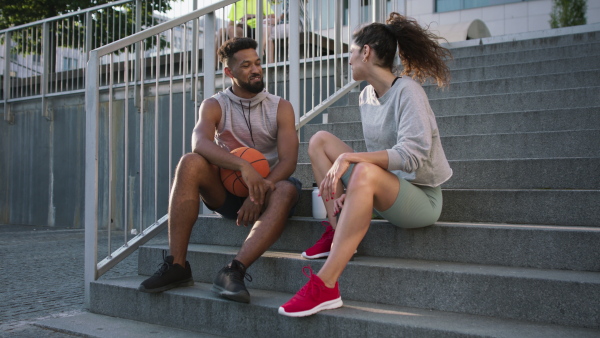 A man and woman friends sitting on stairs outdoors in city, talking after exercise.