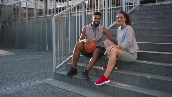 A man and woman friends sitting on stairs outdoors in city, talking after exercise.