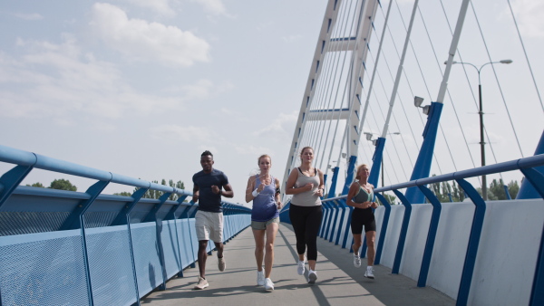 A group of young and old people running outdoors on bridge in city.