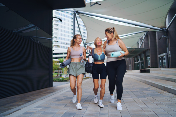 A group of young and old women walking after exercise outdoors in city, talking.