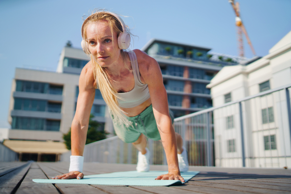 A mid adult woman doing push-ups outdoors in city, exercise and healthy lifestyle concept.