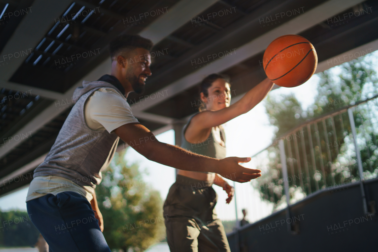 A man and woman friends playing basketball outdoors in city.