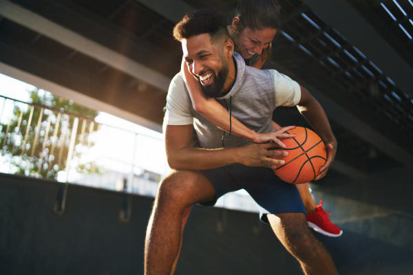 A man and woman friends playing basketball outdoors in city, having fun.