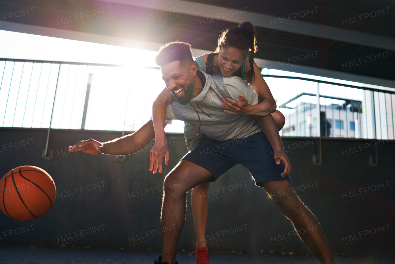 A man and woman friends playing basketball outdoors in city, having fun.