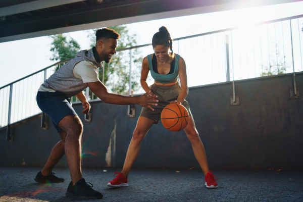 A man and woman friends playing basketball outdoors in city.