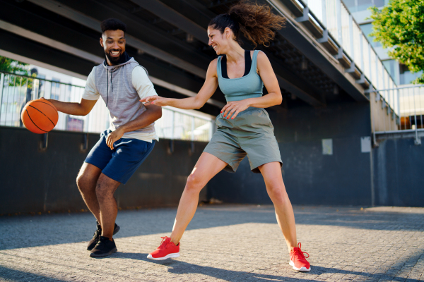 A man and woman friends playing basketball outdoors in city.