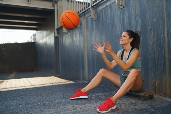 A mid adult woman with basketball outdoors in city, sitting and resting.