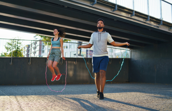 Happy man and woman couple friends doing workout exercise outdoors in city, skipping.