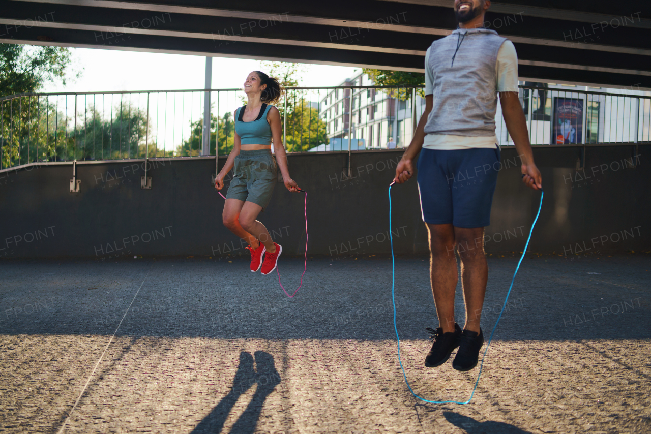 Happy man and woman couple friends doing workout exercise outdoors in city, skipping.