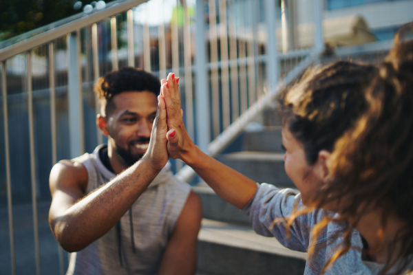 A man and woman friends resting after exercise outdoors in city, giving high five.