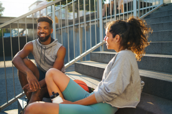 Happy man and woman friends doing exercise outdoors in city, talking.