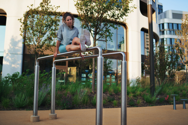 Happy mid adult woman doing exercise on parallel bars outdoors in city, healthy lifestyle concept.