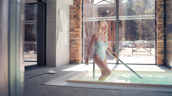 Senior woman walking in indoor swimming pool, healthy lifestyle concept.