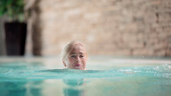 Portrait of happy senior woman in indoor swimming pool, swimming.