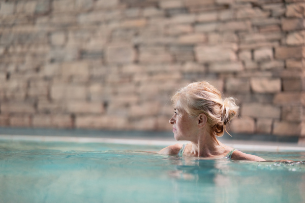 Portrait of happy senior woman in indoor swimming pool, standing.