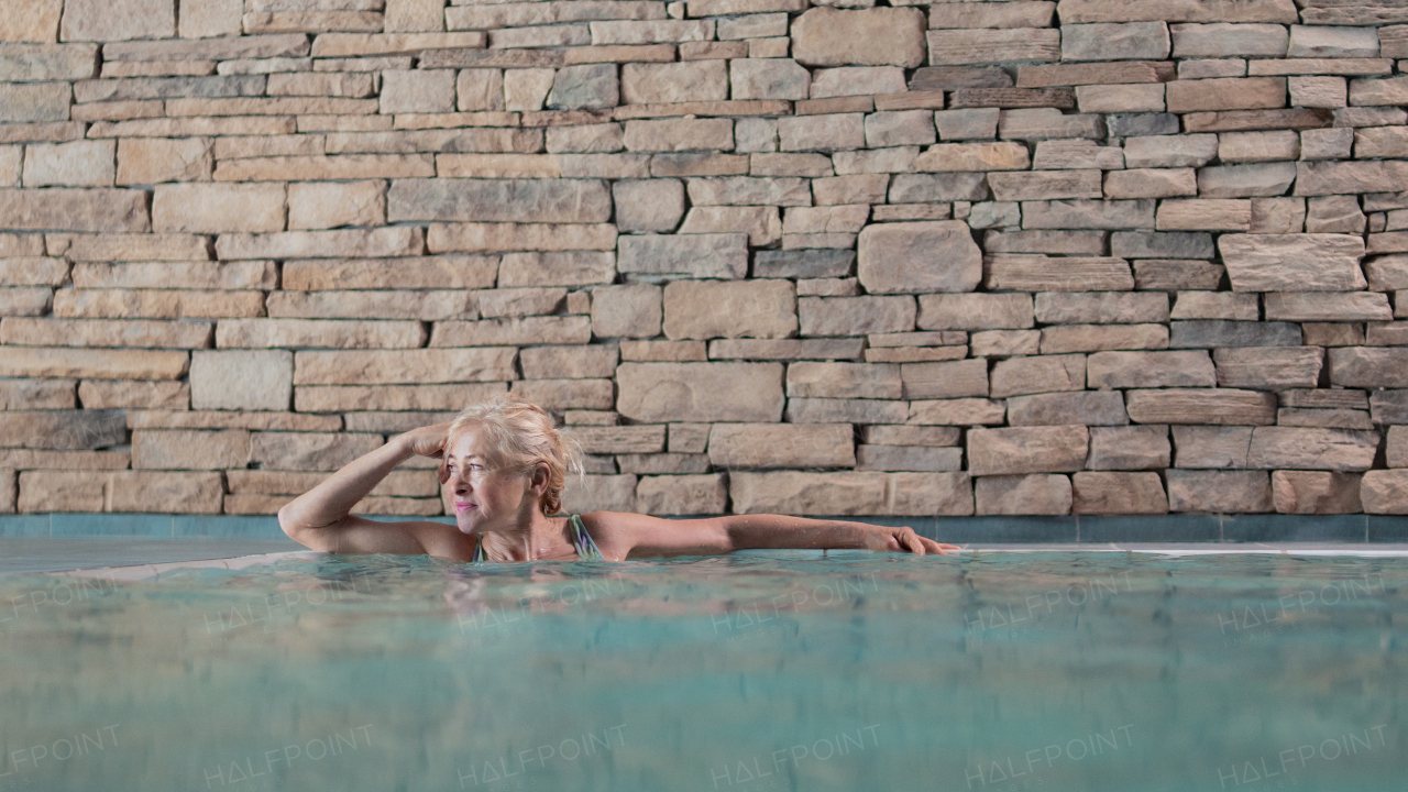 Portrait of happy senior woman in indoor swimming pool, standing.