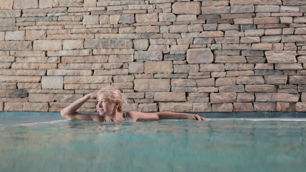 Portrait of happy senior woman in indoor swimming pool, standing.