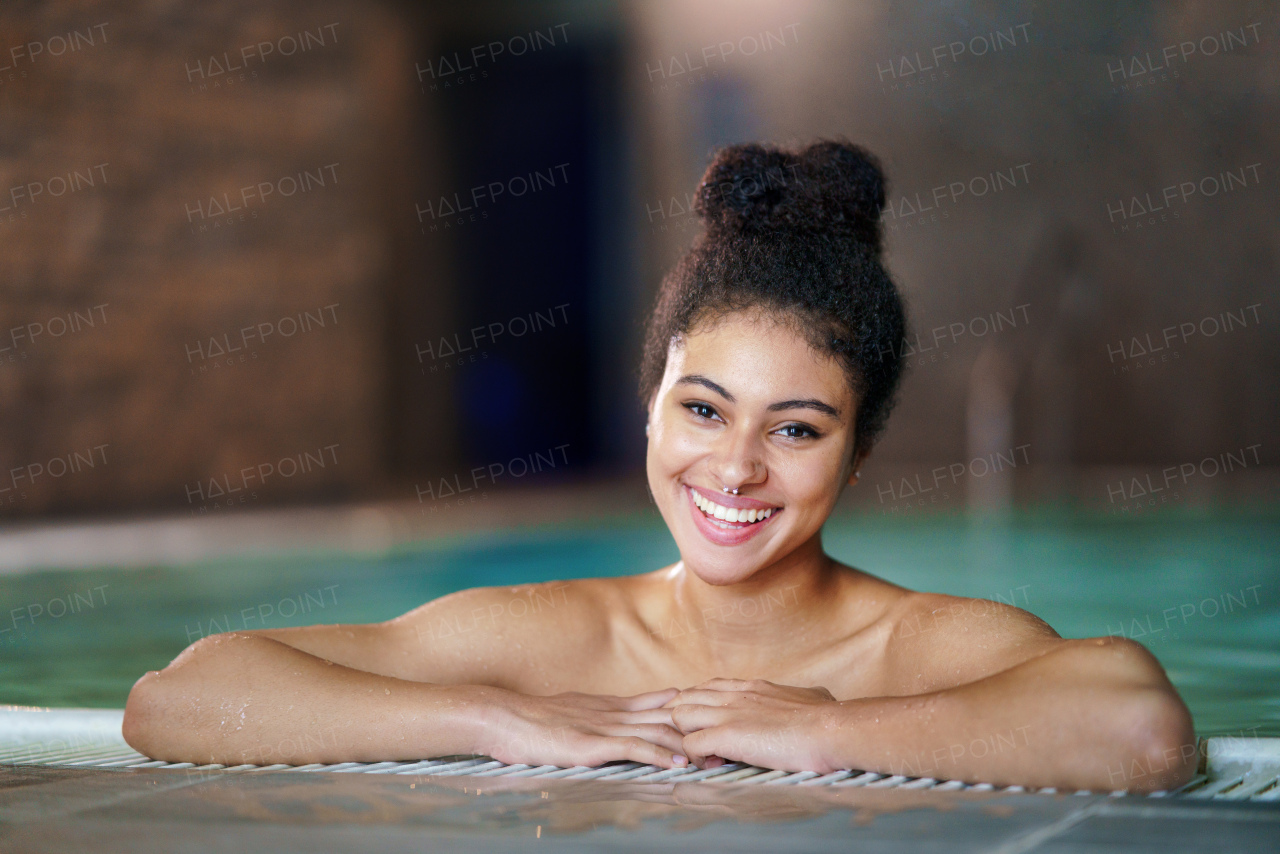 Portrait of happy young woman in indoor swimming pool, looking at camera.