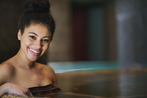 Portrait of happy young woman in indoor hot spring thermal pool, looking at camera.